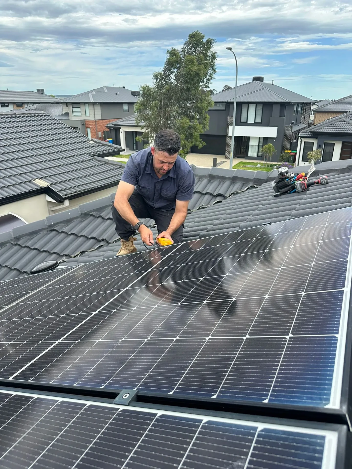 Solar technician testing panels on a tiled roof with a meter